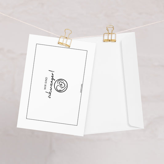 Die Baby-Ankündigungskarte "Wir sind schwanger!" von ohmycard zeigt einen fröhlichen Smiley und den Spruch "WIR SIND schwanger!" auf einer weißen Karte, dazu eine Blankokarte mit Umschlag - beides mit goldenen Klammern an einer Schnur befestigt.