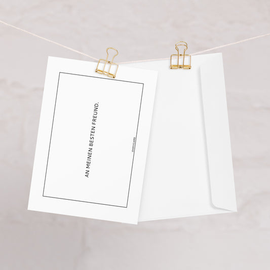 Eine weiße Dankeskarte "An meinen besten Freund" von ohmycard mit deutschem Text hängt zusammen mit dem passenden Umschlag an einer Schnur, beides vor einem sanft verschwommenen Hintergrund.