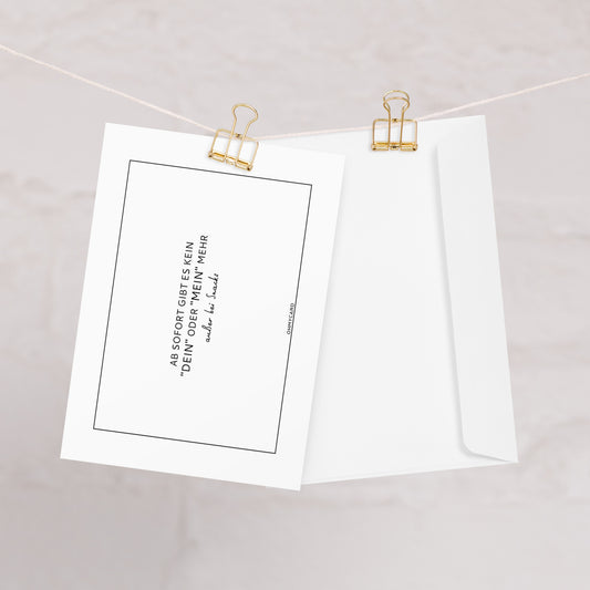 Zwei weiße Karten - eine mit deutschem Text und eine unbedruckte - aus dem Set "kein DEIN oder MEIN" von ohmycard hängen an einer Schnur mit goldenen Binderclips. Ein witziges Hochzeitsgeschenk für frisch verheiratete Paare vor sanftem Hintergrund.