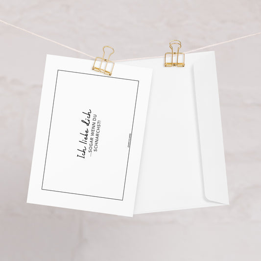 Die ohmycard Karte "Ich liebe dich ... sogar wenn du schnarchst." ist an einer Schnur neben einem weißen Umschlag befestigt - ideal für Partner und schlaflose Nächte.