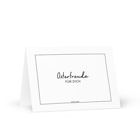 Die Grußkarte "Osterfreude für dich" von ohmycard zeigt den schwarzen Text auf Weiß, umrahmt von einem feinen schwarzen Rechteck. Die Osterkarte steht leicht geöffnet vor weißem Hintergrund.