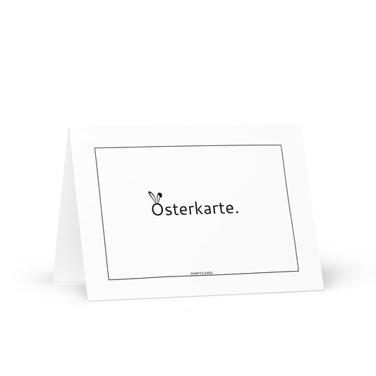 Die Osterkarte von ohmycard ist eine weiße, gefaltete Grußkarte mit dem Schriftzug "Osterkarte." in der Mitte der Vorderseite. Das "O" ist mit Hasenohren versehen, ein schmaler rechteckiger Rand umrahmt das Design und es wird vor einem weißen Hintergrund gezeigt.